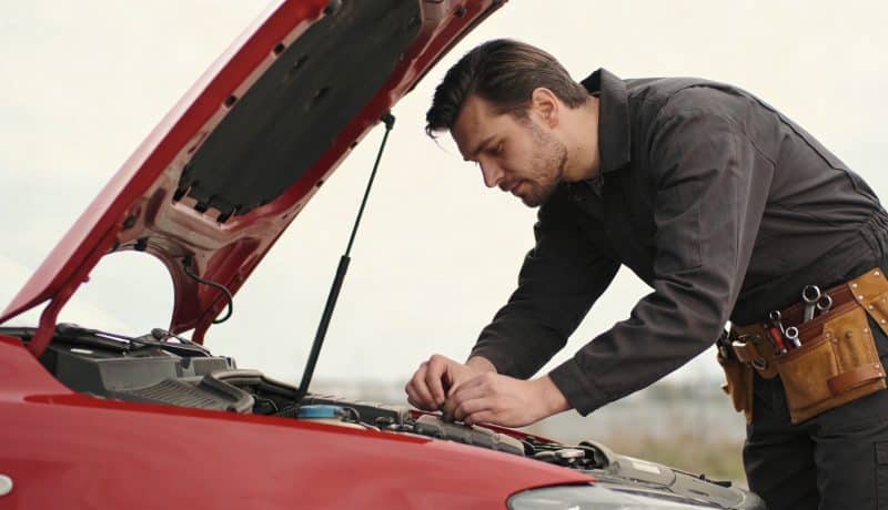 mecanicien penche sous capot de voiture rouge
