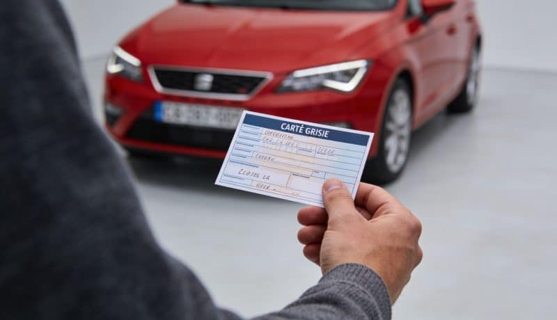 main tenant carte grise avec voiture rouge en arriere plan