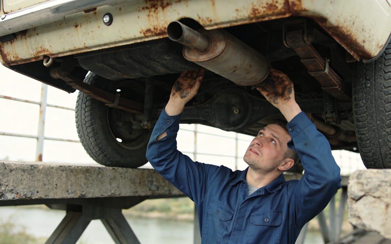 Mecanicien inspectant sous une vieille voiture sur pont